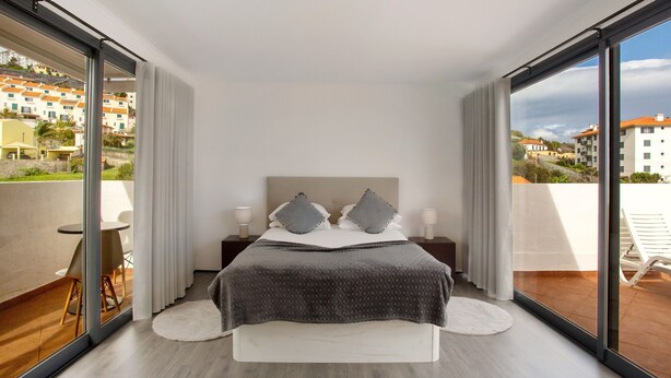 Un dormitorio con cama, mesitas de noche, vistas amplias por ventanas grandes y un balcón.