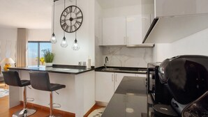 Una cocina moderna con una isla central, taburetes de bar, una cafetera y un reloj en la pared.