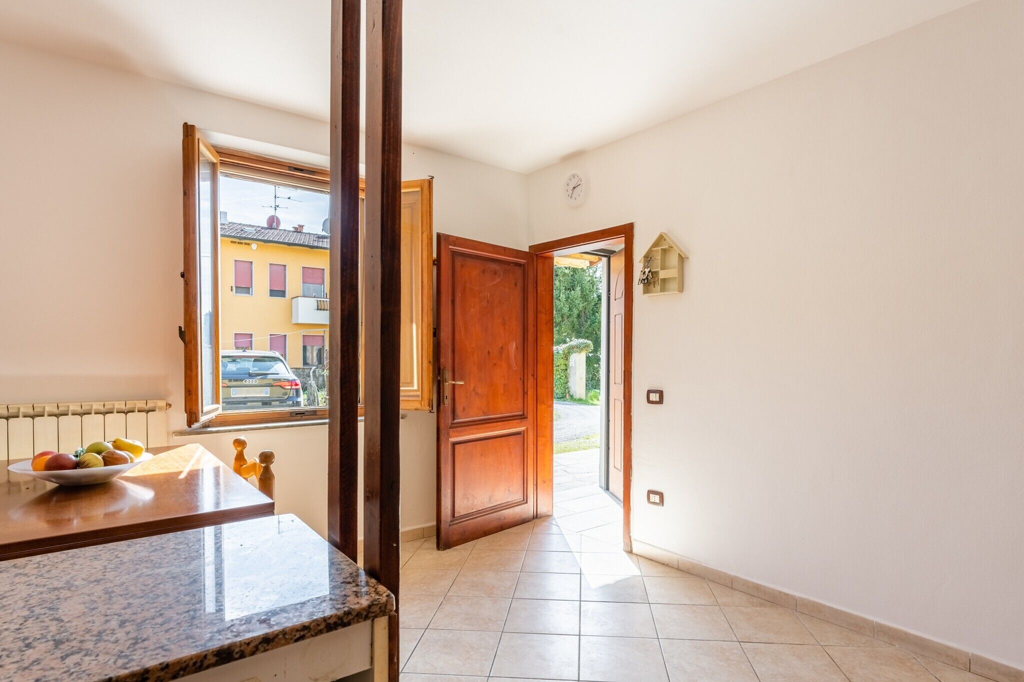 A hallway with a wooden door, a window with a view of buildings, and a tiled floor.