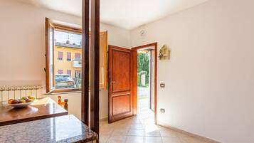 A hallway with a wooden door, a window with a view of buildings, and a tiled floor.