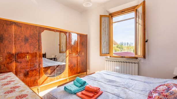 A bedroom with a bed, a large mirror, a window with a view, and a radiator. - Holiday Home 'Enza's Petite Maison' with Wi-Fi (Staffoli)