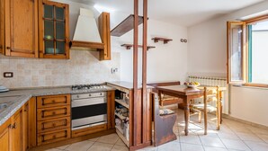 A kitchen with wooden cabinets, a gas stove, an oven, and a dining table with chairs. - Holiday Home 'Enza's Petite Maison' with Wi-Fi (Staffoli)