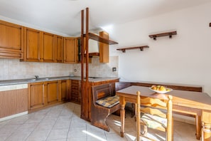 A kitchen with wooden cabinets, a bench, a dining table, and a fruit bowl.