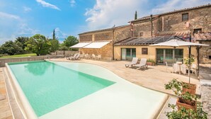 A swimming pool with lounge chairs, a covered patio, and a building with a tiled roof. - Brotes: Chic Apartment in Tuscany, Shared Pool, Hot Tub & Sauna, Wi-Fi, Air Conditioning (Sovicille)