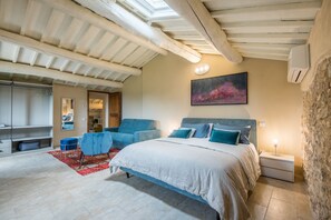 A bedroom with a large bed, a blue armchair, a red rug, and a painting on the wall.