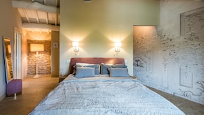 A bedroom with a bed, two wall-mounted lights, a stone wall, and a decorative wall panel.
