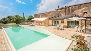 A swimming pool with lounge chairs, a covered patio, and a building with a tiled roof.