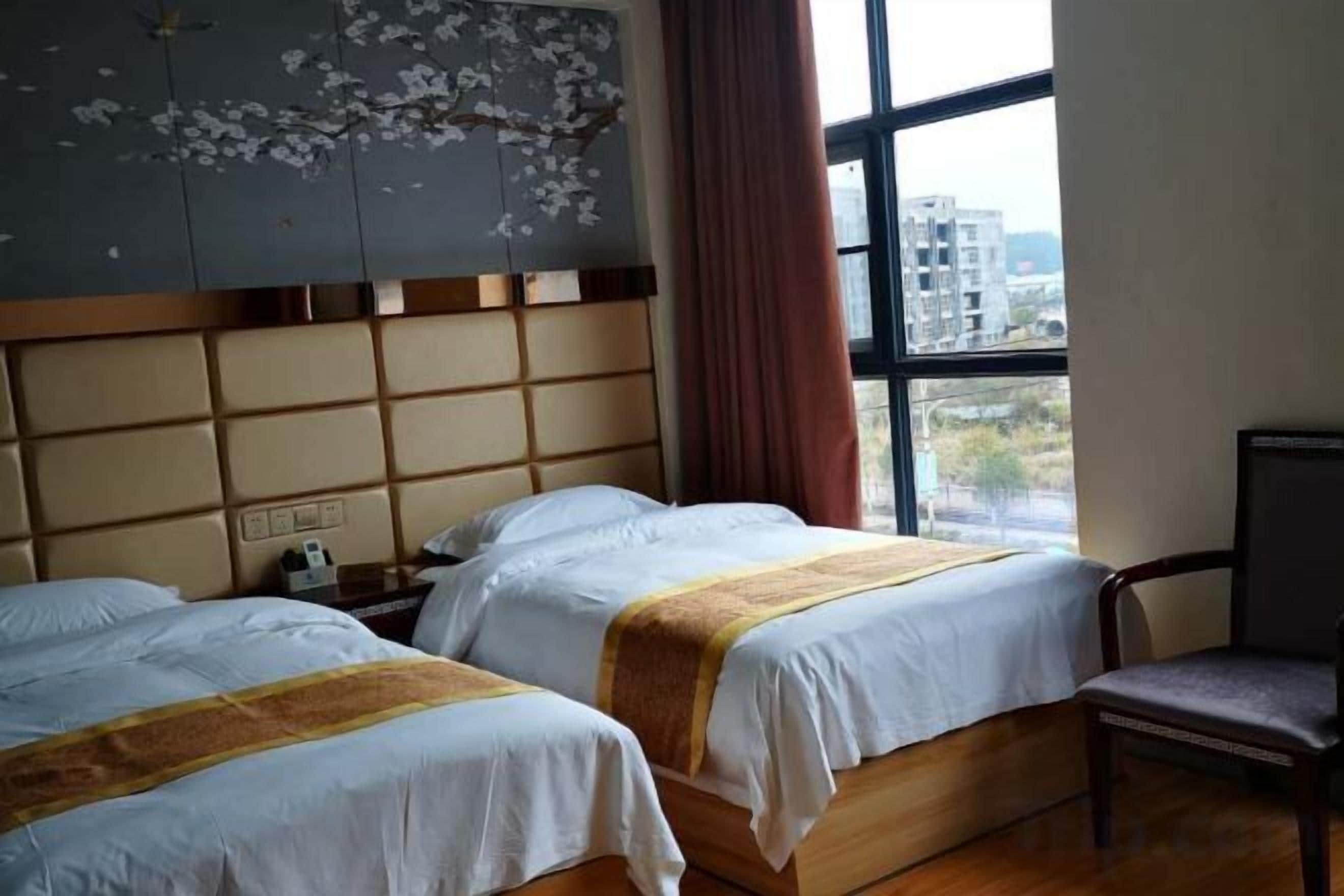 A hotel room with two beds, a wooden headboard, a window with a view, and a chair.