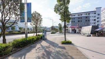 A paved walkway with trees, a building with multiple floors, and a clear sky.