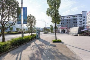 Un camino pavimentado con árboles, un edificio de varios pisos y un cielo despejado.