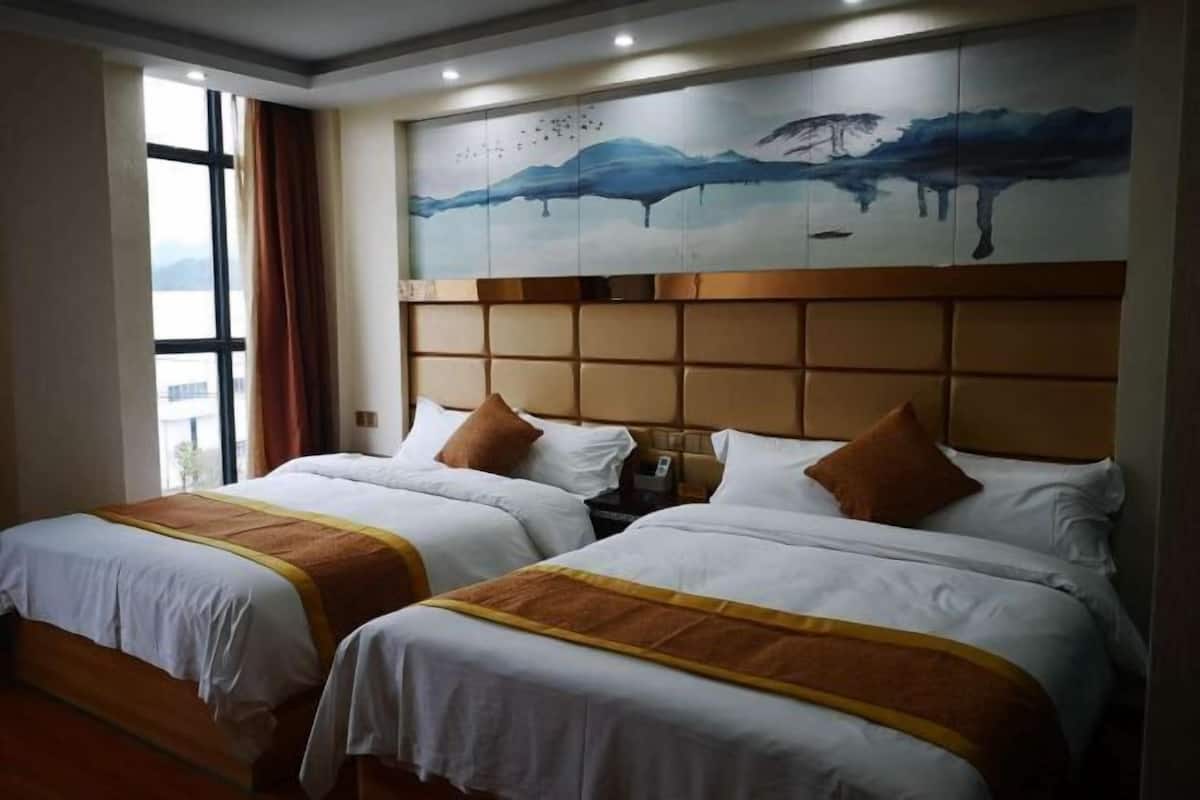 A hotel room with two beds, a large window, and a painting of a mountain landscape on the wall.