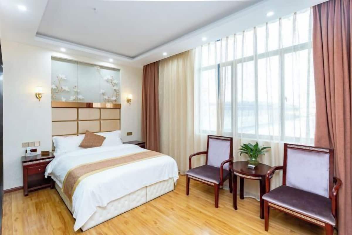 A hotel room with a large bed, two chairs, a small table, and a window with curtains.