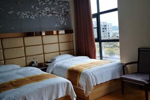 A hotel room with two beds, a wooden headboard, a window with a view of buildings, and a chair. - Xuangui Hotel (Guiding)