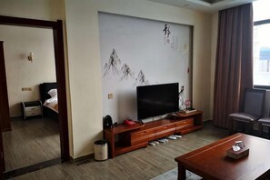 Una sala moderna con un televisor de pantalla plana, mueble de entretenimiento de madera y un amplio ventanal con cortinas.
