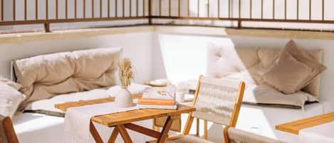 Uma área de estar acolhedora ao ar livre, com móveis de madeira e almofadas, uma mesa pequena com livros e um vaso decorativo.