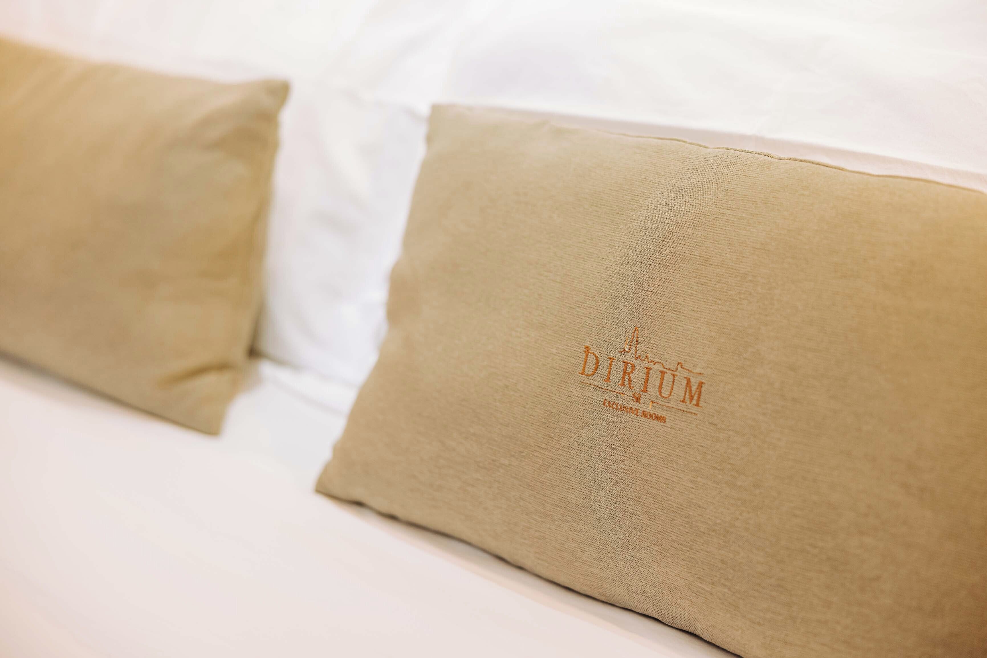 Un lit avec deux oreillers de couleur beige, dont l’un porte un logo.