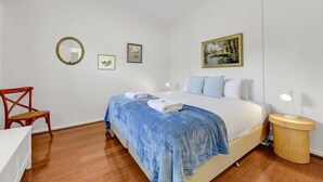 Ein Schlafzimmer mit einem Bett, einem Sessel, einem Nachttisch und einer Wand mit gerahmten Bildern.