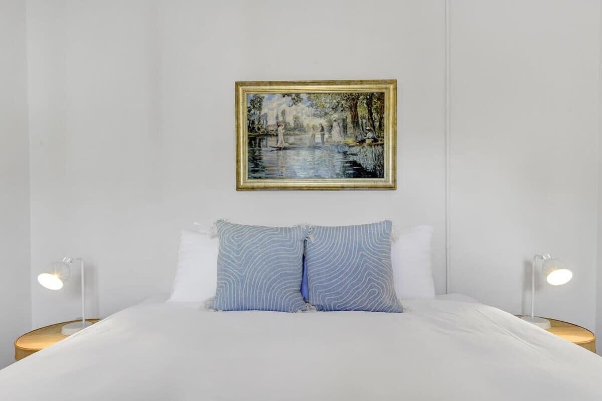 A bedroom with a bed, two bedside tables, a nightstand, and a framed painting on the wall.