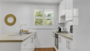 Eine moderne Küche mit weißen Schränken, einer Edelstahl-Spüle und einem Fenster mit Jalousien.