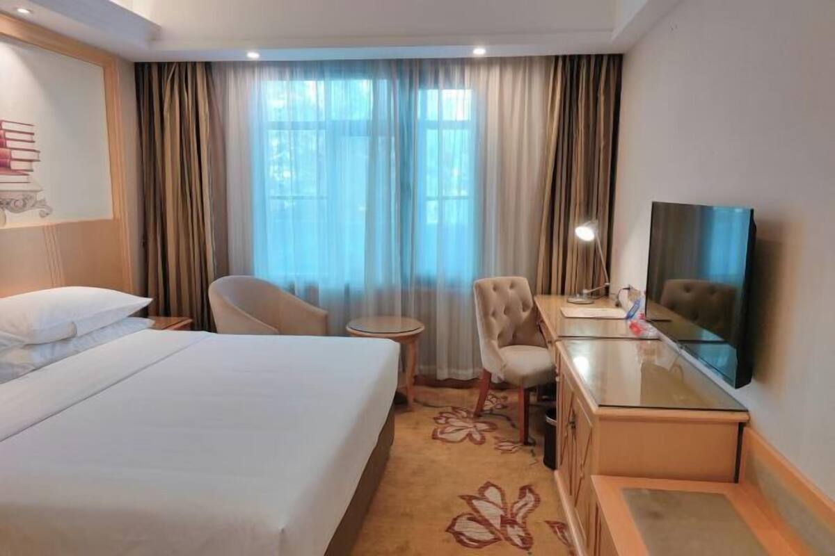 A hotel room with a bed, a desk, a chair, a TV, and a window with curtains.