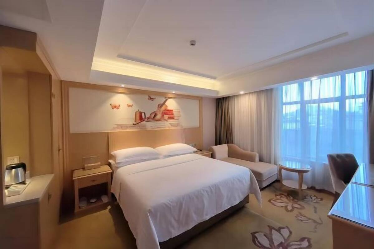 A hotel room with a bed, a sofa, a small table, and a window with curtains.