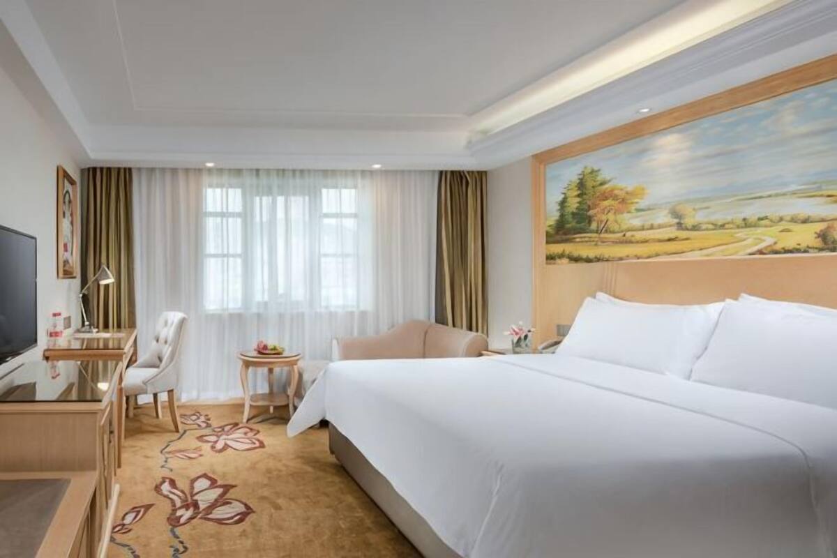 A hotel room with a large bed, a desk with a chair, a television, and a painting on the wall.