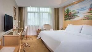 A hotel room with a large bed, a desk with a chair, a television, and a painting on the wall.