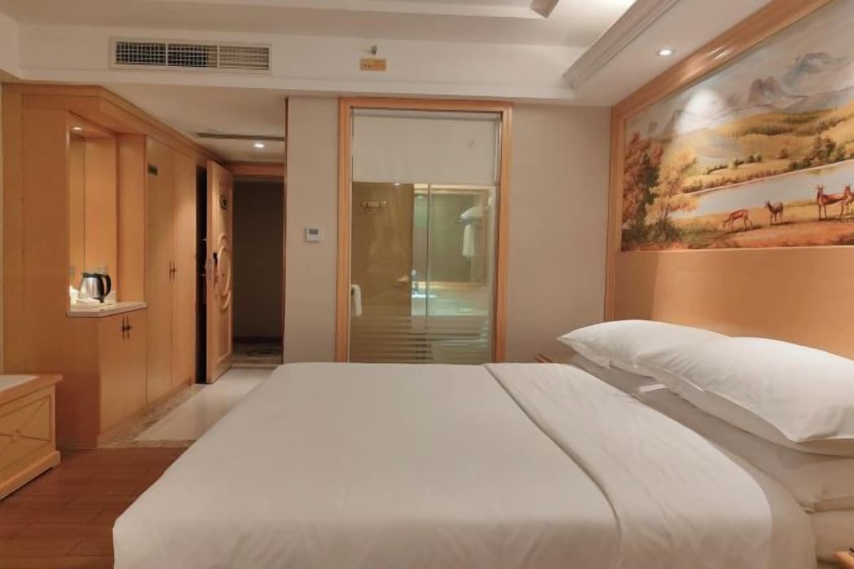 Een hotelkamer met een bed, een houten kledingkast en een schilderij van een landschap aan de muur.