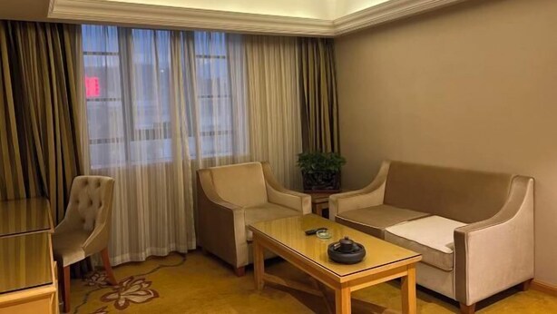 A hotel room with a sofa, armchair, small table, and a potted plant.