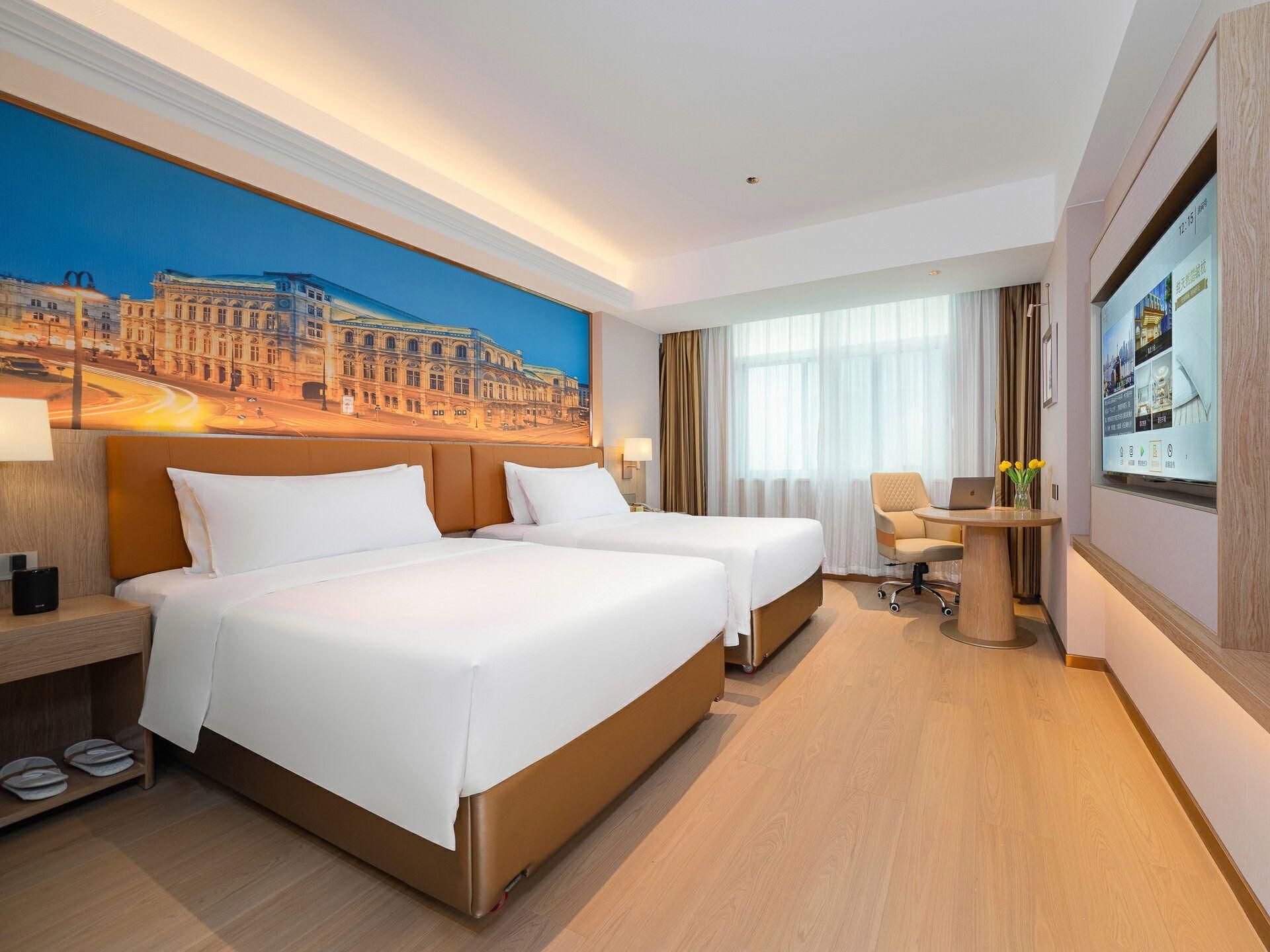 A hotel room with two beds, a desk, a chair, a laptop, and a large window with curtains.