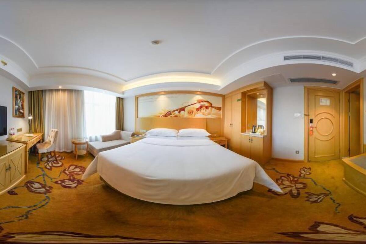 A hotel room with a large bed, a desk with a chair, a small table, and a TV.