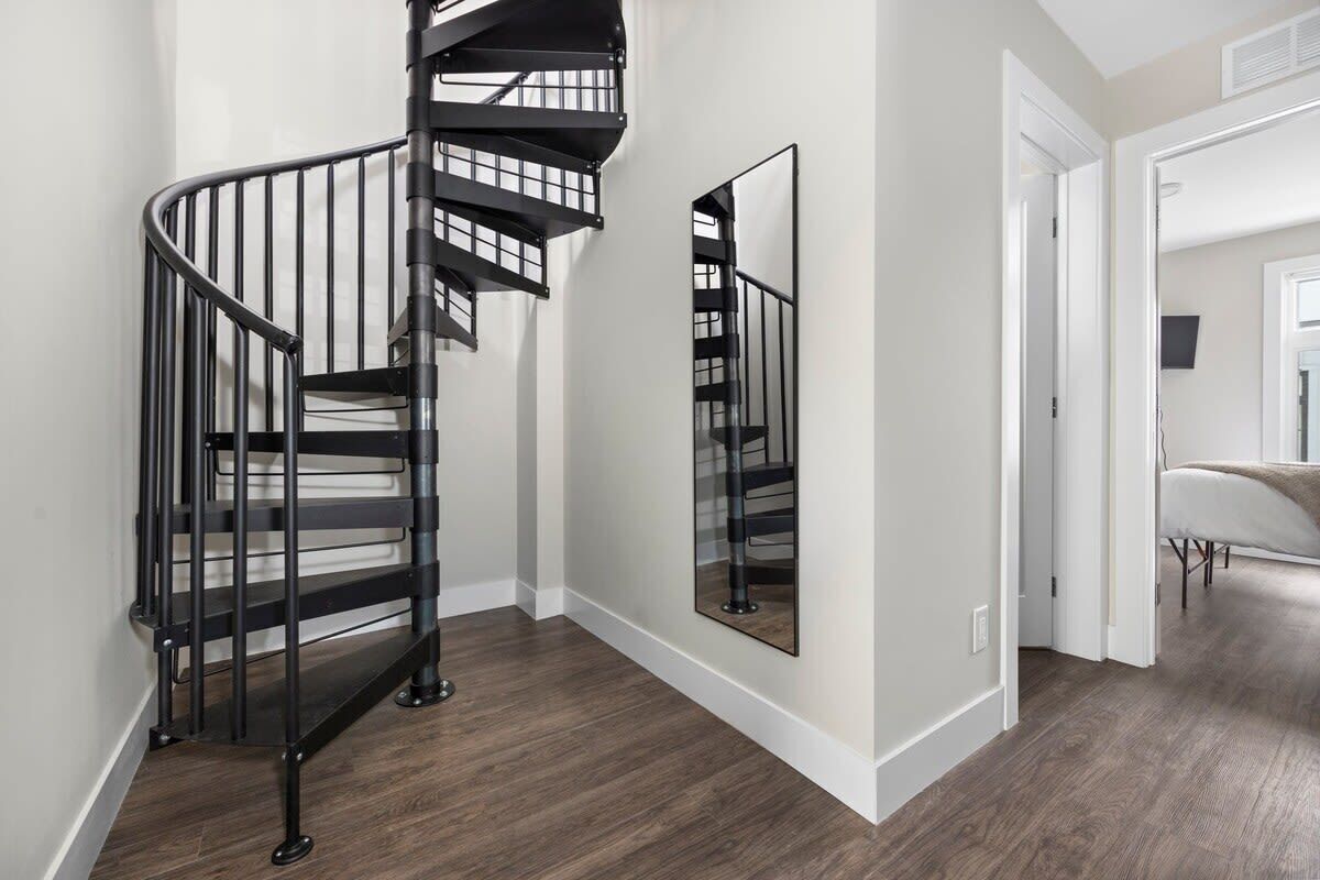 Un intérieur moderne avec un escalier en colimaçon, un miroir qui reflète l’escalier et un couloir menant à une autre pièce.