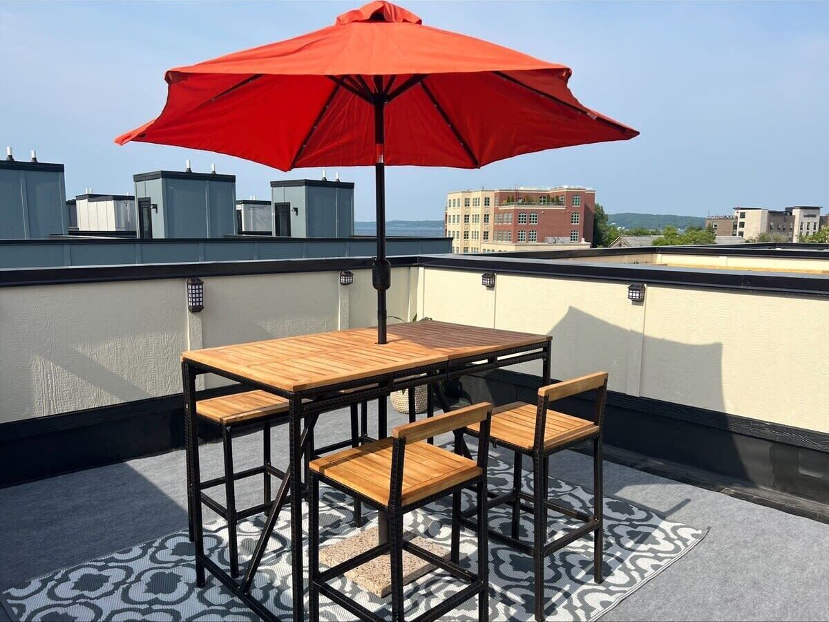 Une terrasse sur le toit avec une table et des chaises en bois, un parasol rouge et un tapis à motifs.
