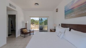 A spacious bedroom with a large bed, a chair, and a view of the outdoors through a sliding door. - Ocean View, Pool, Private Beach! (Cabo Bello)