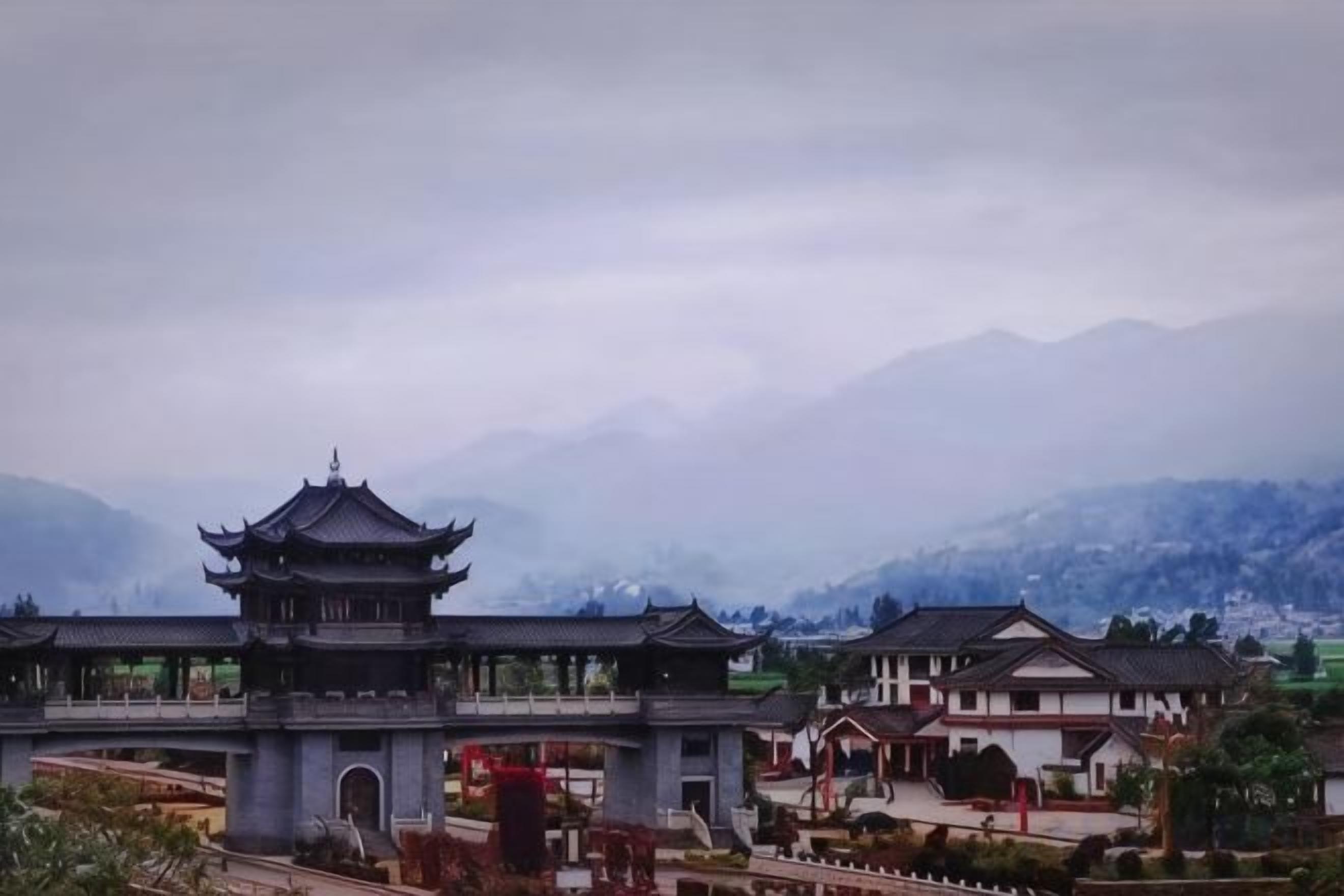 Un edifici xinès tradicional amb un teulat de diversos nivells, envoltat de muntanyes i un cel nuvolós.