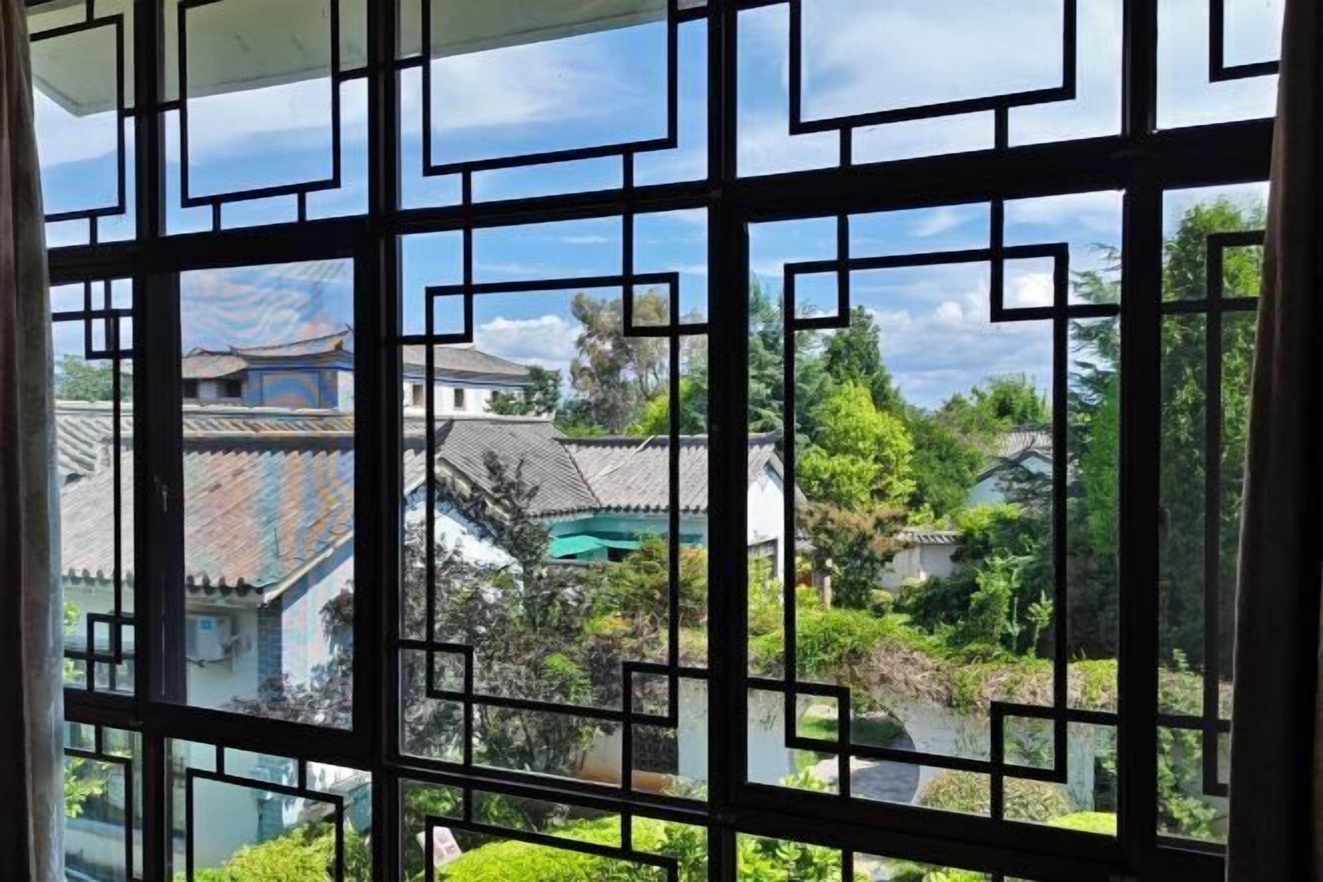Ein traditionelles Fenster mit geometrischen Mustern, Blick auf Gebäude mit Ziegeldächern und üppiges Grün.