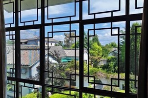 A traditional window with geometric patterns, a view of buildings with tiled roofs, and lush greenery.