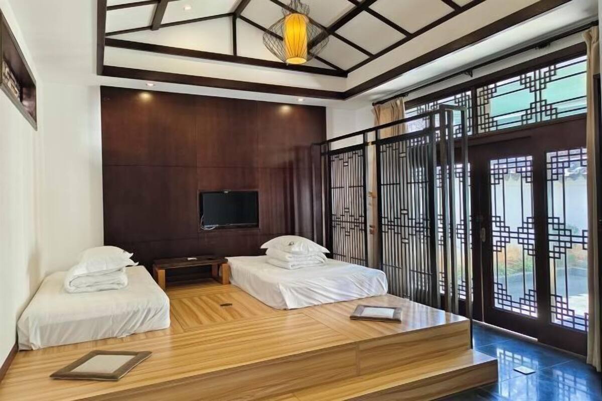 Ein Zimmer mit zwei Betten, einer Holzplattform, einem Fernseher und einem großen Fenster mit Blick.