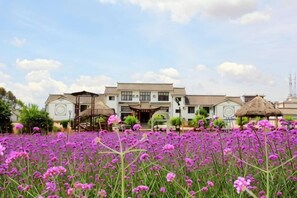 A traditional building with a symmetrical facade, a central entrance with a covered walkway, and a field of purple flowers in the foreground.