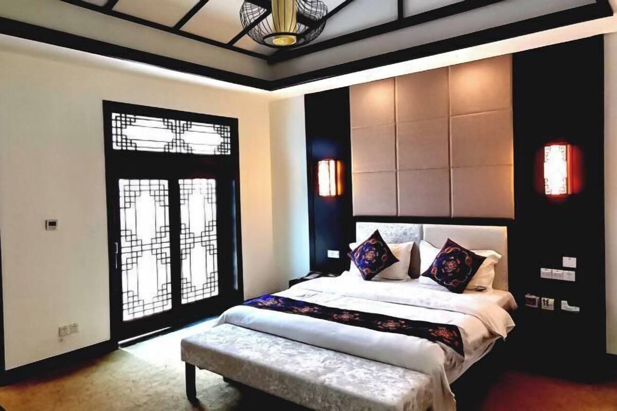 Ein Schlafzimmer mit Bett, einer Bank, einer Wandleuchte und einer Tür mit geometrischem Muster.