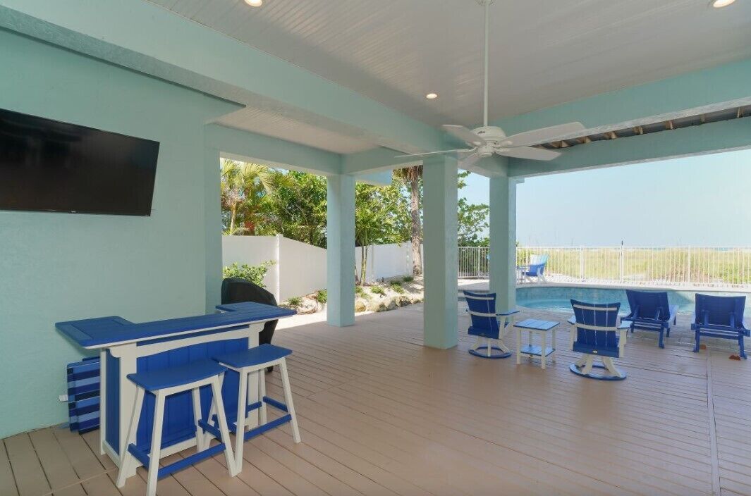 Ein überdachter Außenbereich mit Pool, blauen Möbeln und einem Deckenventilator.