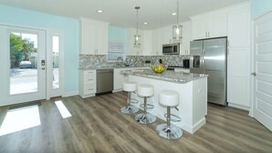 A modern kitchen with white cabinets, stainless steel appliances, and a central island with bar stools. - Bean Point Beachfront- Beachfront 4 bedroom private home with pool/spa (Anna Maria)