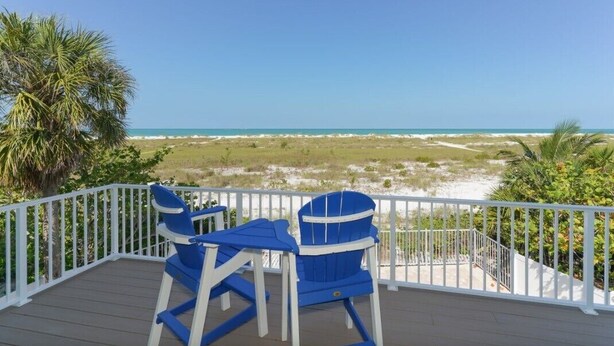 A deck with blue chairs and a table overlooking a beach with dunes and ocean. - Bean Point Beachfront- Beachfront 4 bedroom private home with pool/spa (Anna Maria)