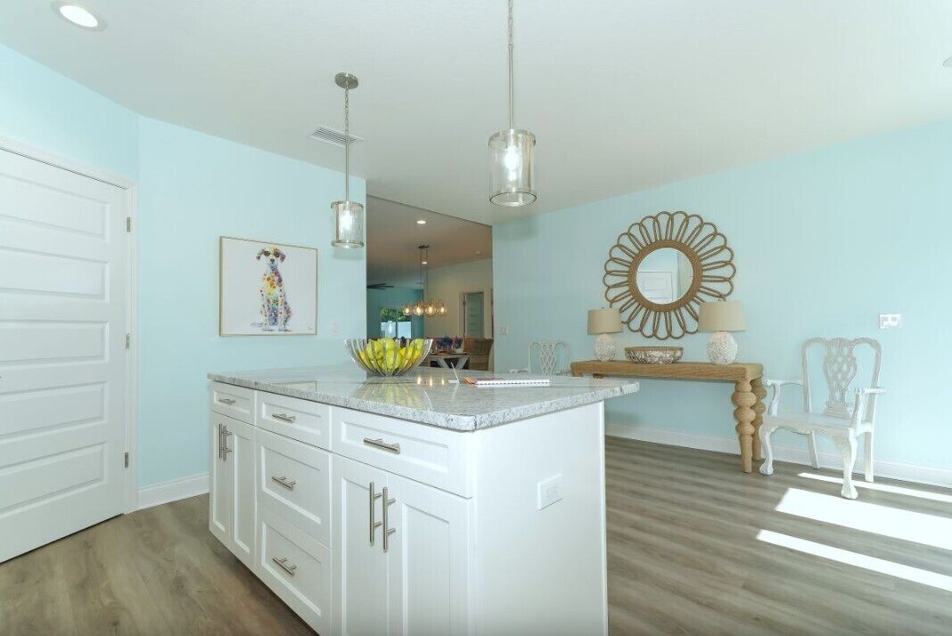 A modern kitchen with white cabinetry, a central island, pendant lighting, and a decorative mirror.