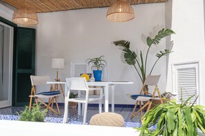 Een kamer met een witte tafel, twee witte stoelen, een rieten lamp, een potplant en een blauwe emmer.
