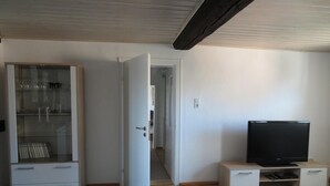 A room with a glass-fronted cabinet, a television on a wooden stand, and a door leading to another room. - Apartment Oels Witzenhausen OG incl. balcony (Witzenhausen)