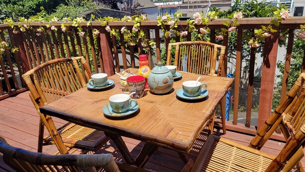 Une terrasse en bois avec une table dressée pour quatre personnes, entourée de chaises en bambou.