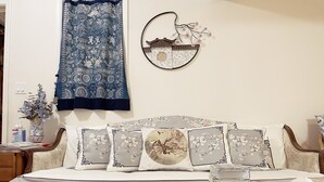 Une chambre à coucher bien rangée, avec un lit, des oreillers, une table de chevet, un vase de fleurs, une décoration murale et une petite table sur laquelle se trouve un panier contenant une télécommande et un téléphone.