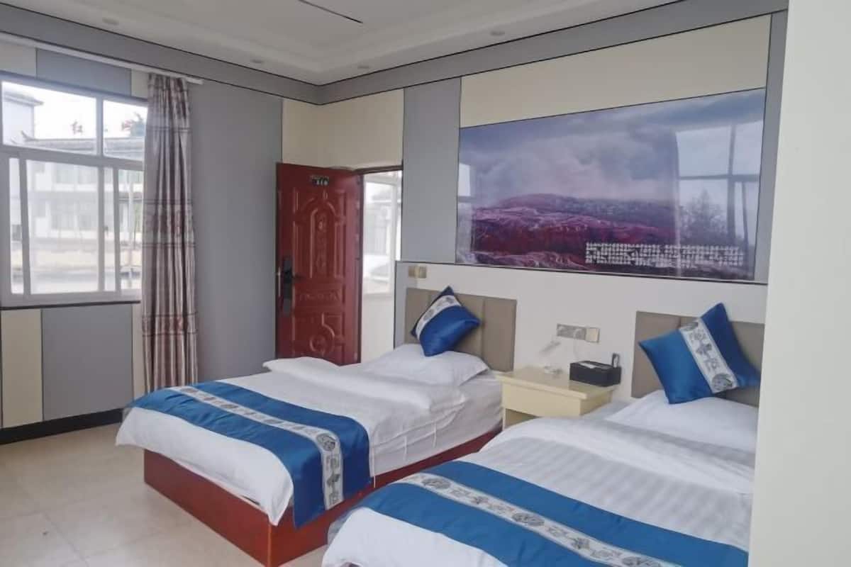 A hotel room with two beds, a large window, a door, and a painting on the wall.