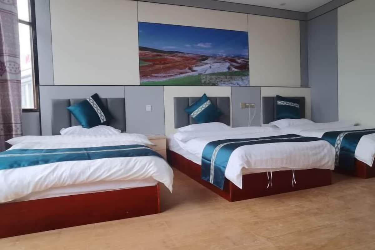A hotel room with two beds, a large landscape painting above the beds, and a window with curtains.